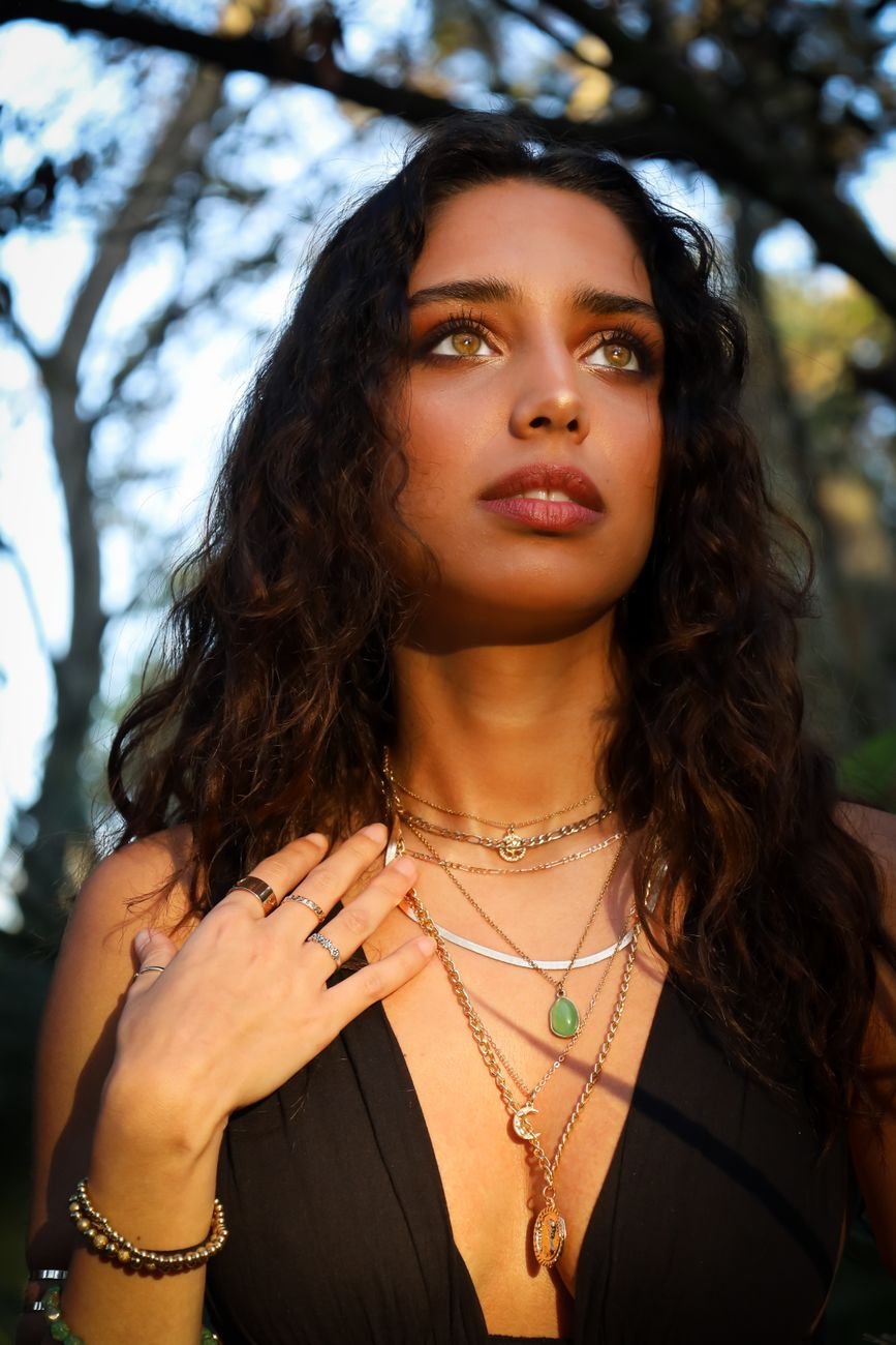 A captivating outdoor portrait of a woman wearing layered jewelry, showcasing a serene expression in natural light.