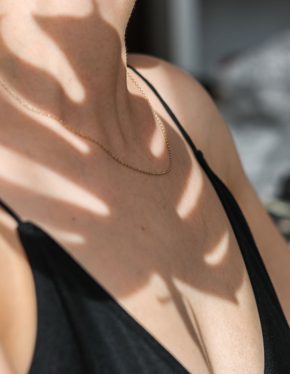 Close-up of a woman's neck with a gold necklace and artistic shadows on skin.